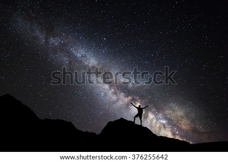 Landscape with Milky Way. Night sky with stars and silhouette of a standing happy man with raised up arms on the mountain.