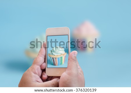 Point of view of woman taking a photo of her cupcake with her smartphone. Picture of food on screen.