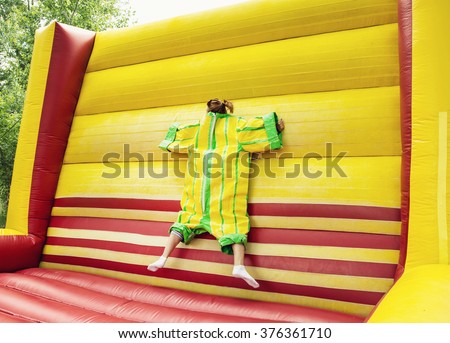 Young woman in plastic dress in a bouncy castle imitates a fly on velcro wall. Inflatable attraction. Leisure activity. Royalty-Free Stock Photo #376361710