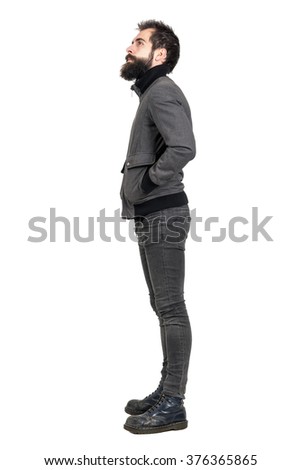 Side view of young bearded punker in old army boots looking up with hands in pockets. Full body length portrait isolated over white studio background. 
