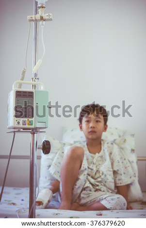 Illness asian boy sitting on sickbed in hospital with infusion pump intravenous IV drip. Shallow depth of field (DOF) IV machine in focus, child out of focus. Retro style.