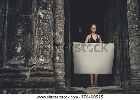 Young woman holding blank placard in dark mystic location