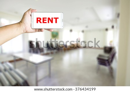 Man holding a mobile phone ,blur image of midsize conference room as background.