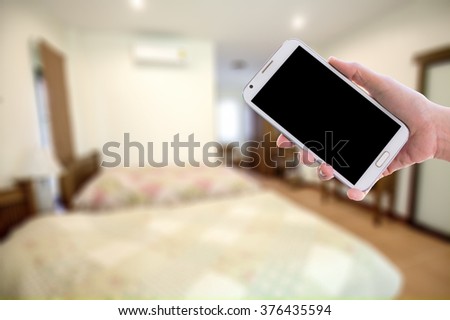 Man holding a mobile phone ,blur image of guestroom as background.