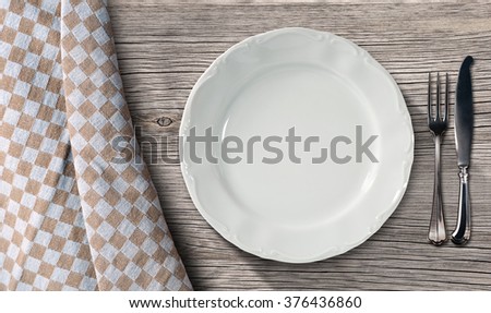 Empty plate on a table in pine wood with silver cutlery, fork and knife, and a brown and white checkered tablecloth 