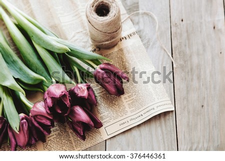 Spring tulips flowers wrapped in craft paper and twine on rough wooden table, selective focus, rustic eco style