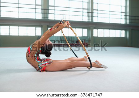Little girl in beautiful gymnastic dress doing exercise with hoop on floor