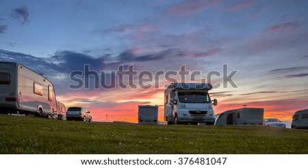 Caravans and cars parked on a grassy campground in summer under beautiful sunset Royalty-Free Stock Photo #376481047