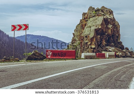 Roadside red and white triple chevron sign warning for dangerous road turn on sinuous Transfagarasan highway, Romania.