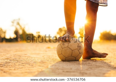 Close up picture of an old ball and foot of a boy who is playing football in the sunshine day.