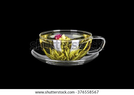 Green tea with red flower in transparent glass cup on saucer, studio shot, isolated on black 