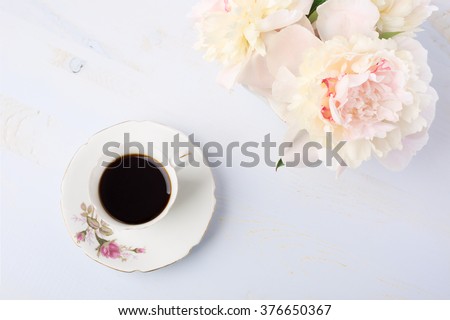Still life with cup of coffee and flowers (peonies) on light  lilac wooden table.