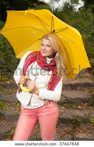 Picture of a young happy blond girl under a yellow umbrella in an autumn park