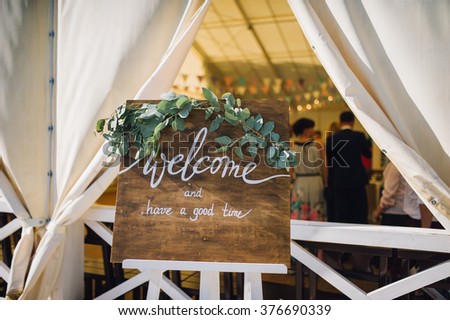 handmade wooden board with welcome sign on it decorated with eucalyptus on white stand with candlelight on background