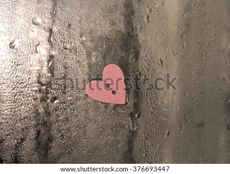 The wooden button in the shape of a heart on the window with drops of water,the button on the background of a wet window,sewing button scrap booking heart love on a rainy day window background,vintage