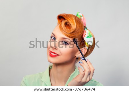 Taking care of eyebrows. Closeup portrait red head beautiful attractive girl woman retro pin up bow hair style with eyebrow brush tool green formal shirt isolated grey background wall. Beauty stylist 