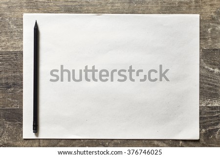 Black pencil on a sheet of paper to the left on a dark wooden background