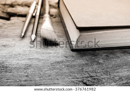 book, pencil, pen and paintbrush on a old wooden table