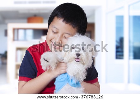 Picture of a funny little boy hugging a maltese dog at home while smiling happy
