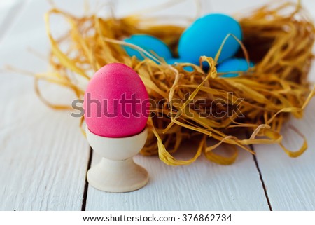 blue and pink Easter eggs in nest on white wooden background