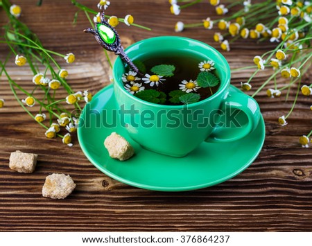 tea with a chamomile and herbs in a green mug on a wooden background