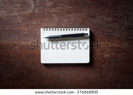 Small opened notepad with blank area for text or message and pen on rustic wood table with low key scene.