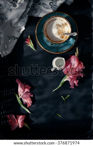 Cup of cappuccino set with pink flowers, contrast morning natural lighting, dark style photo, overview. Romantic background with retro filter effect. Toned photo.