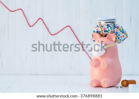 A pink piggy bank, that is sick, sits on antique, white wooden boards. Yarn is placed slightly out of focus in the background to give a representation of the stock market crashing.