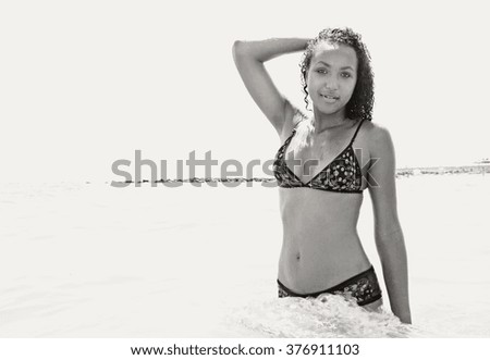Black and white view of beautiful african american teenager young woman bathing in the sea on a sunny summer holiday, coastal exterior. Adolescent travel lifestyle, in sunny clear water beach.