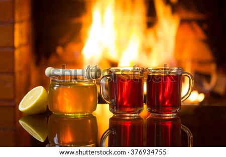 Two cups of hot drink, bowl of honey and lemon in front of warm fireplace. Magical relaxed cozy atmosphere near fire.