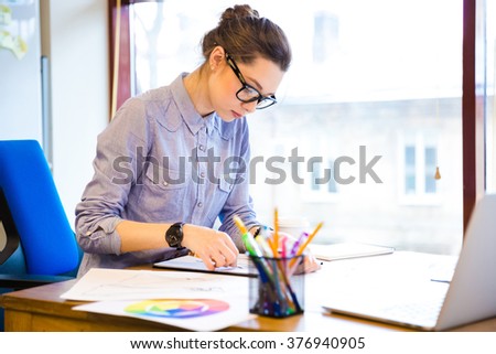 Concentrated pretty young woman fashion designer sitting and drawing sketches in office