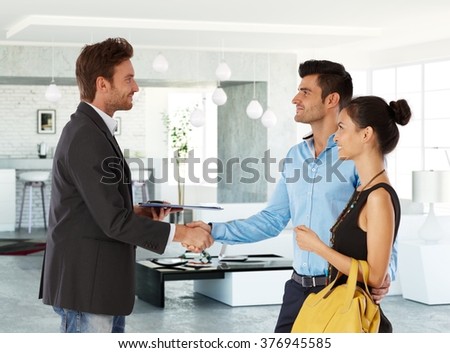 Young couple and real estate agent shaking hands, smiling. Side view.