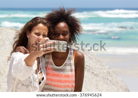 Portrait of two smiling young women taking selfie at the beach