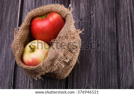 Burlap sack full of big beautiful ripe red and yellow apples on grey wooden timber background, horizontal picture