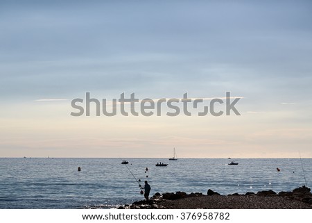 Beautiful evening marine fisherman and vessels offshore in calm blue sea silhouetted against milky cloudy sky on seascape background, horizontal picture