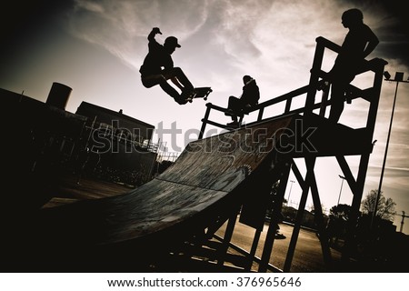 Skateboarder jumping on a ramp. Backlight makes dark silhouettes. Royalty-Free Stock Photo #376965646