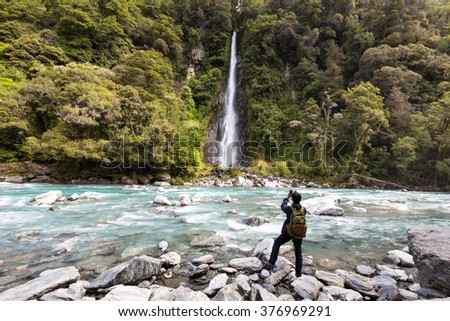 Rear of Tourist man ready to shoot photos at a waterfall and the blue color river with a rocks after trail  in the forest