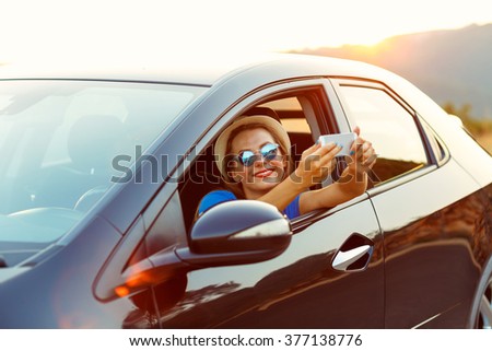Young smiling woman in hat and sunglasses making self portrait sitting in the car