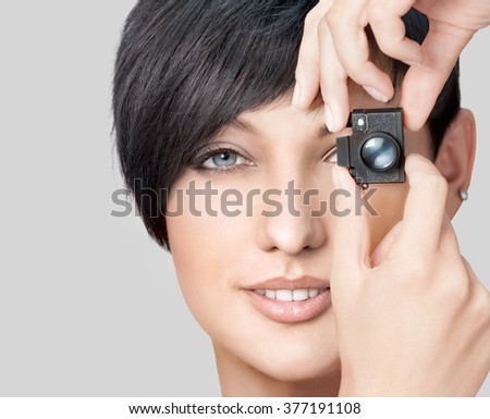 Portrait of pretty young woman holding toy photo camera over gray background