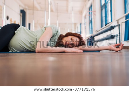 Pregnant woman lying on the floor with eyes closed in a fitness room