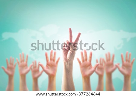 Leader's two fingers victory sign among blur hands crowd group: Many people blurred palms raising up upward on vintage blue sky background map: World participation, leadership volunteer concept: V day