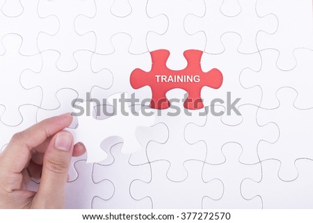 Hand embed missing a piece of puzzle into place, red space with word TRAINING concept