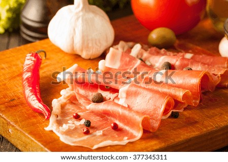 Closeup macro photo of thin slices of prosciutto with green olives, spices and food background on wooden cutting board. Raw dried meat.