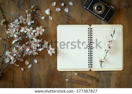 top view image of spring white cherry blossoms tree, open blank notebook, old camera on wooden table
