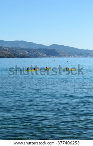 Group of people rowing yellow canoes paddling in beautiful clear calm blue sea with ripples pebble seabed seaside mountains summer day on seascape background, vertical picture