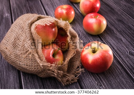 Bright fresh sweet red yellow apples fall out of homespun burlap sack on grey wooden table, horizontal photo