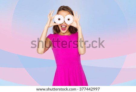 people, holidays, junk food and fast food concept - happy young woman or teen girl in pink dress having fun and looking through donuts over pink violet background