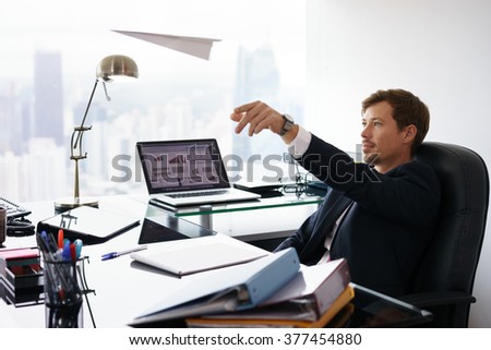 Corporate manager in modern office takes a break and prepares a paper airplane. The bored man dreams of his next vacations and leans back on his chair