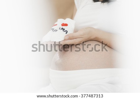 Pregnant woman holding small baby shoes relaxing at home on couch in thailand