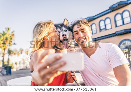 Happy couple taking a selfie with their husky - Woman holding cellphone and taking a funny picture with his family